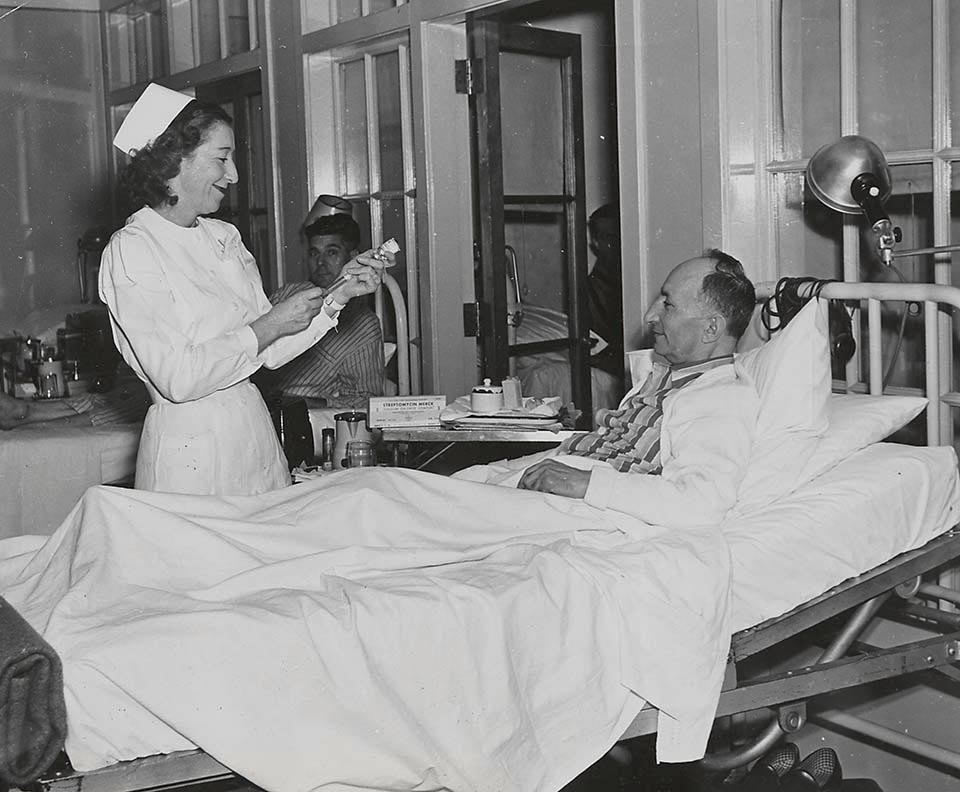 Nurse prepares syringe to give dose to patient in hospital bed