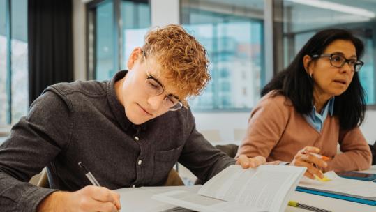 two students in classroom taking notes