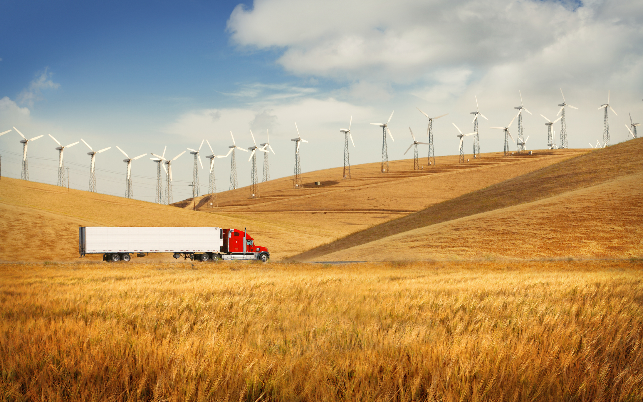 Truck traveling through wheat field with wind mills