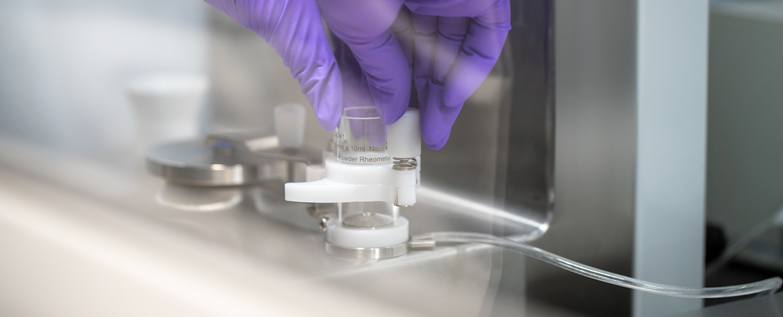 Gloved hand handling a small laboratory device labeled