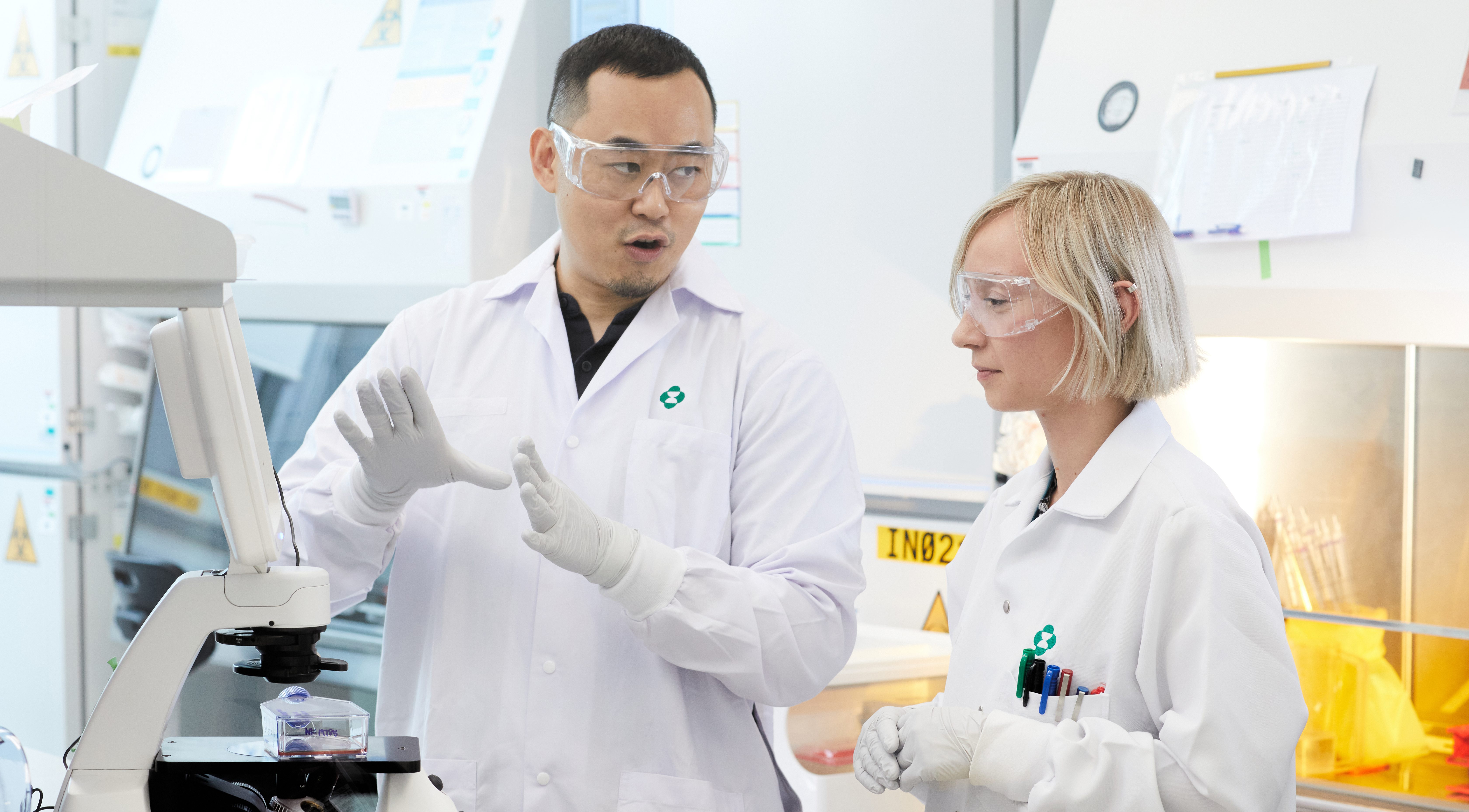 two scientists wearing lab coats and gloves working in a lab